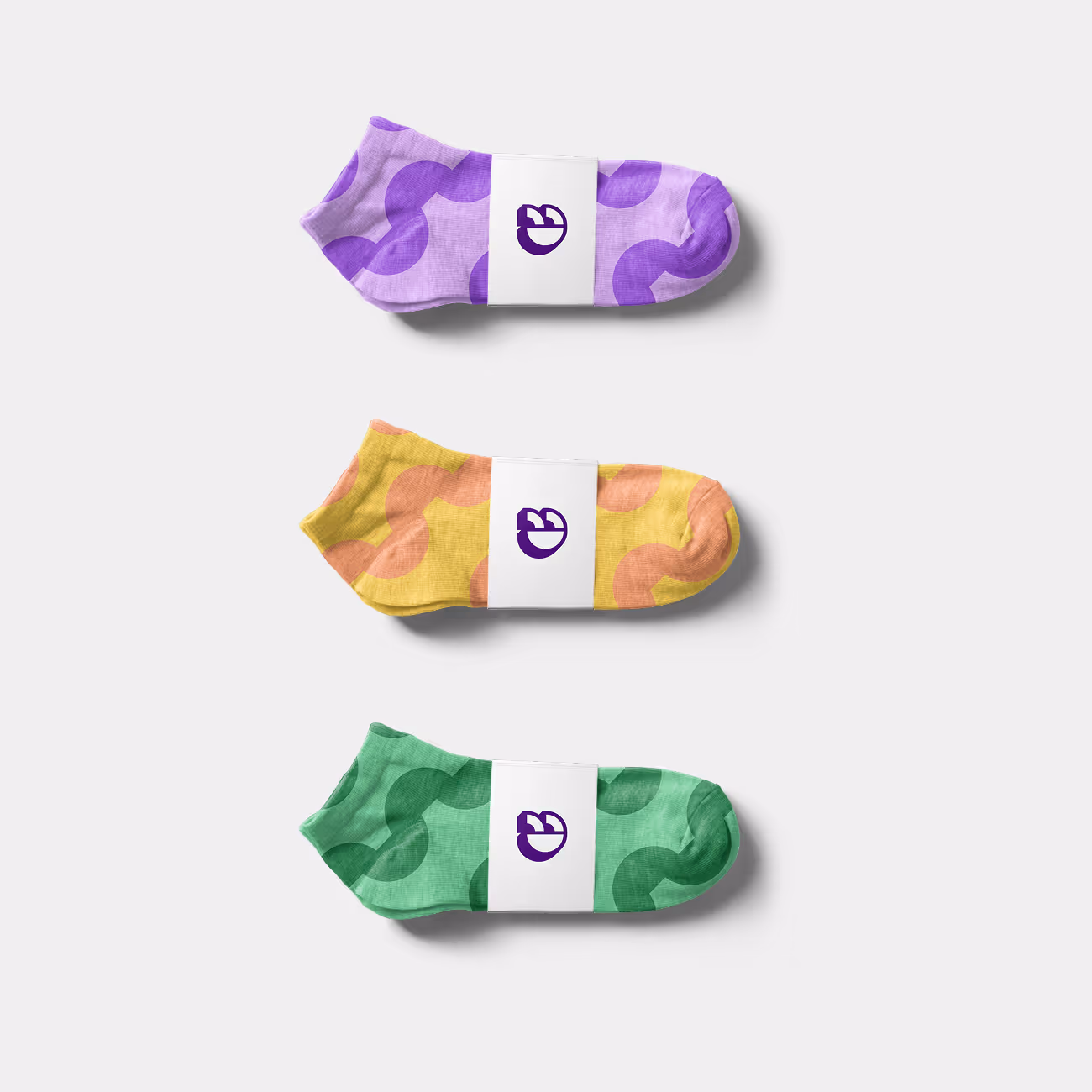 Three pairs of patterned ankle socks in purple, yellow, and green, each wrapped with a white band featuring a purple logo.