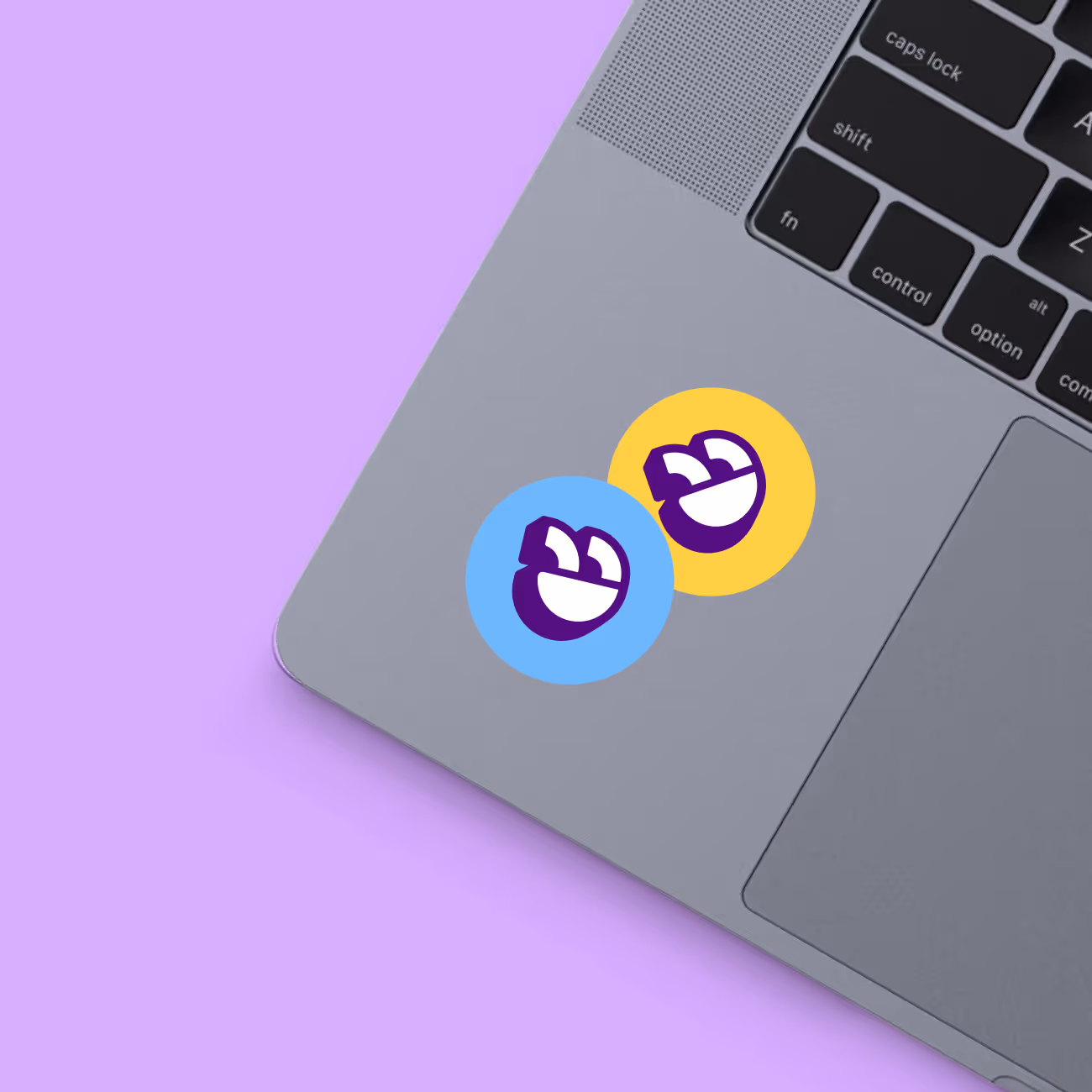 Close-up of a laptop keyboard area with two colorful round stickers featuring a purple and white smiling face icon on blue and yellow backgrounds.