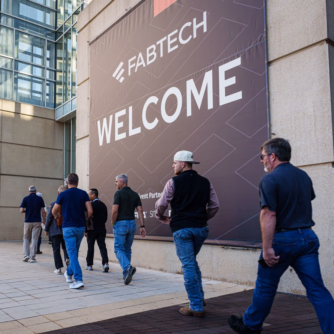 People walking towards a large Fabtech welcome banner on a building wall.