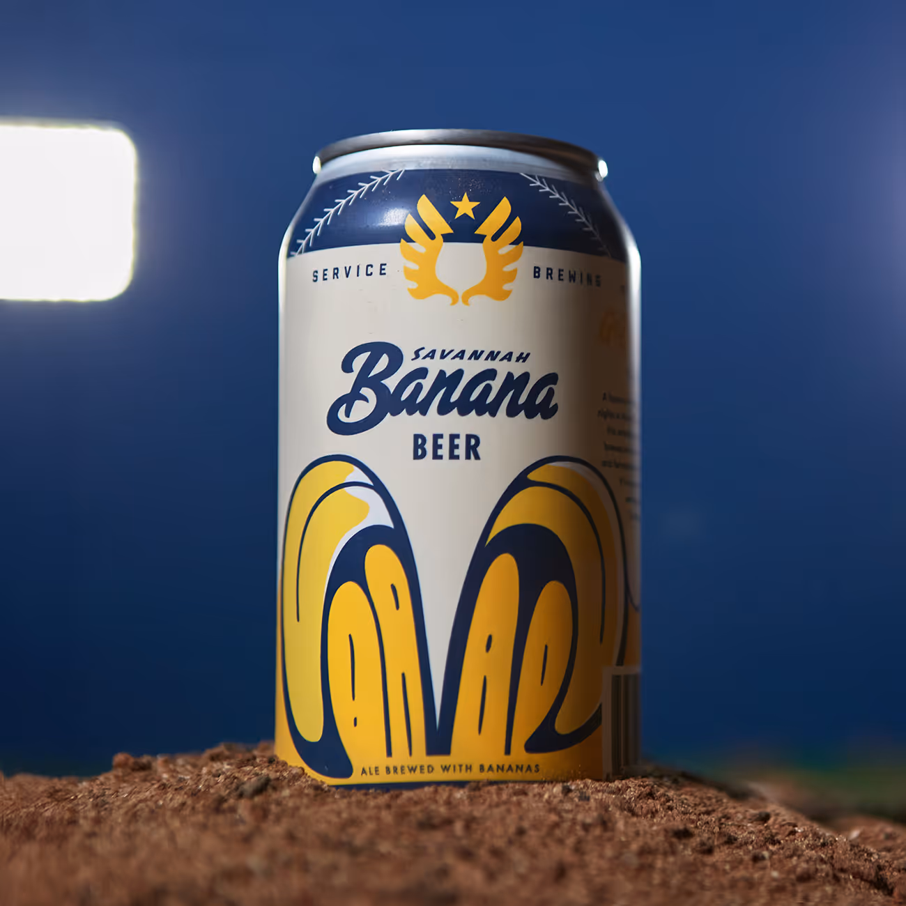 Can of Savannah Banana Beer with blue and yellow design sitting on soil against a blue background.