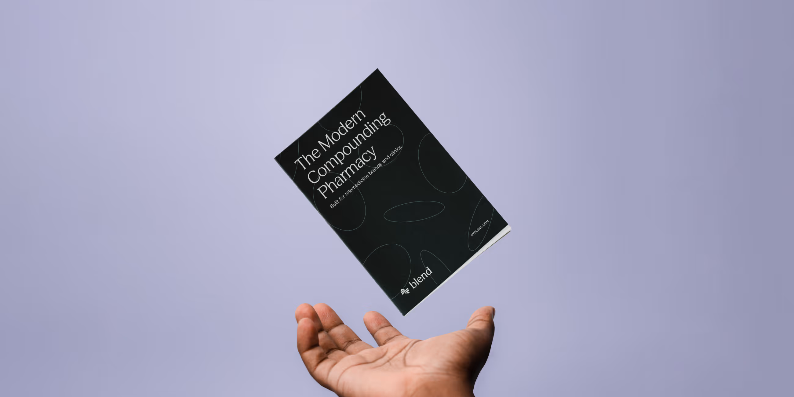 Hand tossing a black booklet titled 'The Modern Compounding Pharmacy' against a plain light purple background.