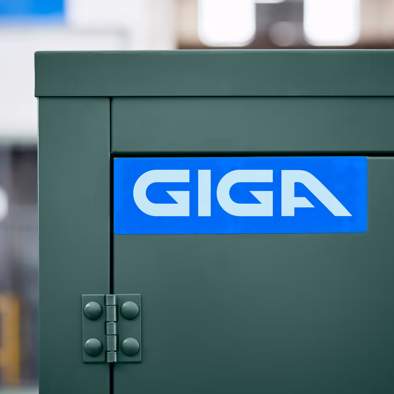 Blue rectangular sign with white text 'GIGA' on a dark green metal cabinet door with hinge visible.