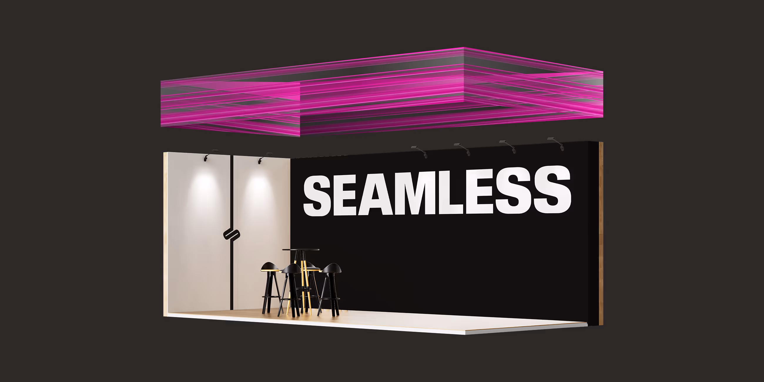 Minimalist tradeshow booth with black wall displaying 'SEAMLESS' in white letters and tall stools.
