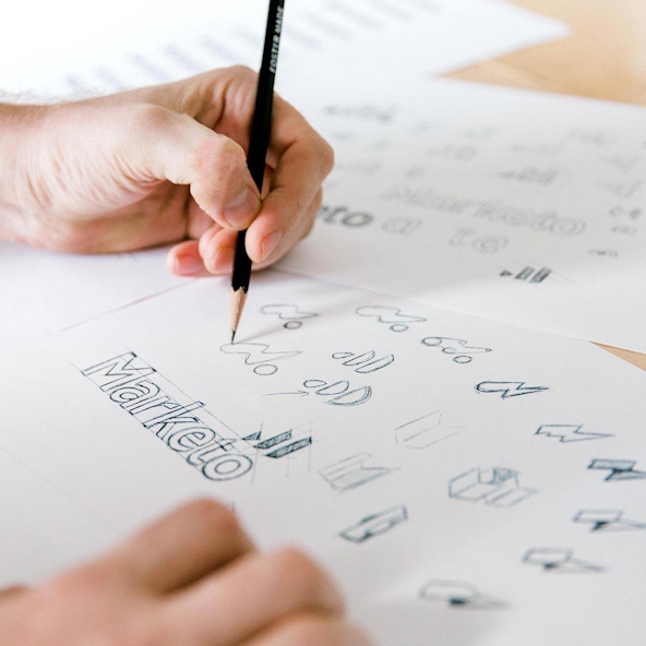 A hand sketches out ideas for Marketo's mark.